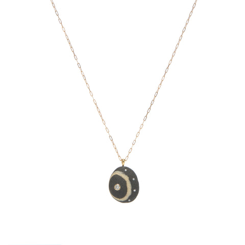 A black stone pendant with a cream wring, accented by one larger diamond and four small diamonds, suspended from a yellow gold paperclip chain. 