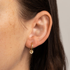Woman wearing a small, yellow gold hoop earring with three yellow gold annulets, one pave with white diamonds. 