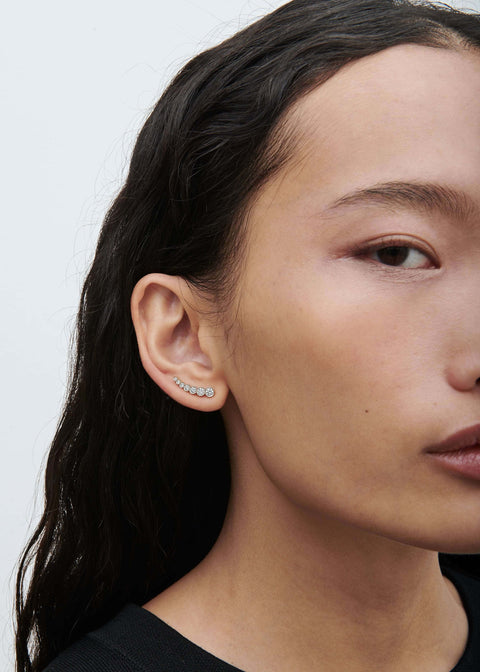 Close-up of a person wearing diamond earrings with a plain background