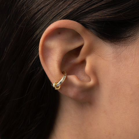 Woman wearing a yellow gold ear cuff with channel set diamonds and a yellow gold annulet. 