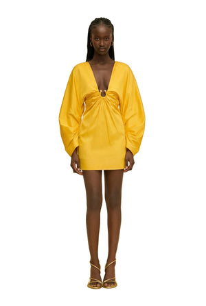 Woman wearing a yellow dress with a cinched ring under the bust against a beige background