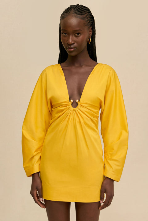 Detail shot of woman wearing a yellow dress with a cinched ring under the bust against a beige background