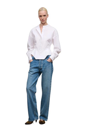 A model wearing a white long-sleeve button-up shirt tucked into blue jeans, standing against a plain white background.