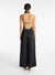 Model facing the back in the black satin pleated jumpsuit, showing the open back and thin strap detail