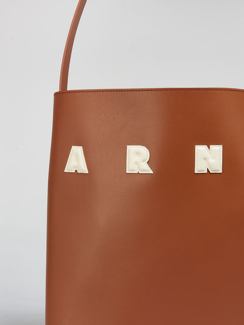 Up close of white letter patches on the small brown leather tote.