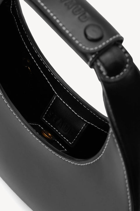 Inside view of a small, black leather, moon shaped handbag with white stitching that magnetic closure. 