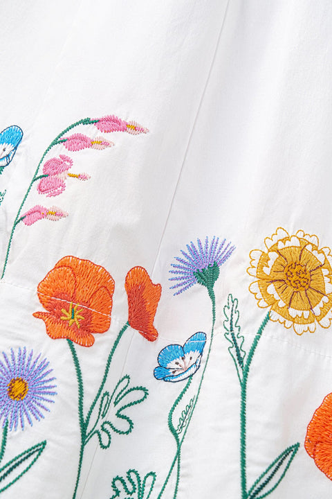 Detail shot of the colorful floral embroidery at the bottom of a white midi dress. 