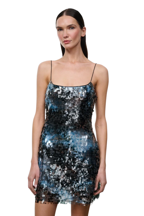 A woman modeling a short spaghetti-strap mini dress covered in shimmering sequins that blend black, silver, and blue tones, set against a plain white background.