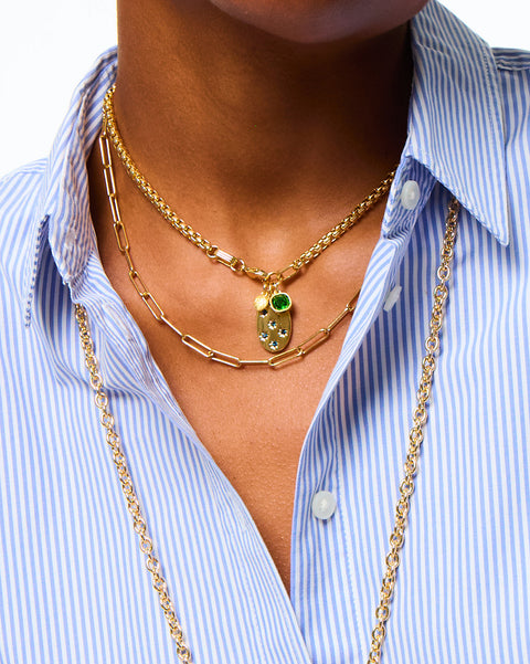 Woman wearing a gold-tone chain necklace that features a star-set sapphire pendant with an emerald charm. 