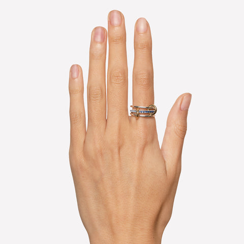 A woman's hand wearing a a Spinelli Kilcollin linked ring that features two thin sterling silver rings connected to a sterling silver ring that is paved with ombre light to dark blue sapphires, connected with to 18k yellow gold connector rings on her index finger. 