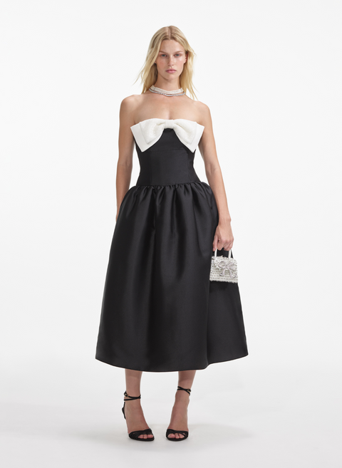 Woman wears black strapless midi dress with white bow on the chest.