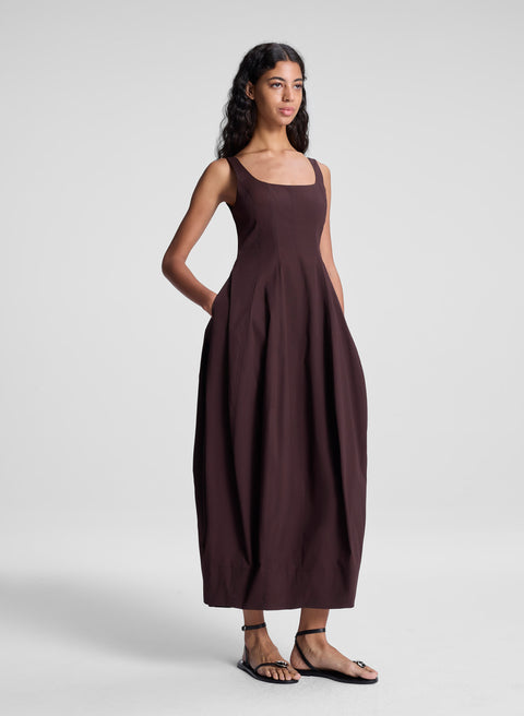 Woman turned with hand in pockets wearing a brown midi dress on a white background