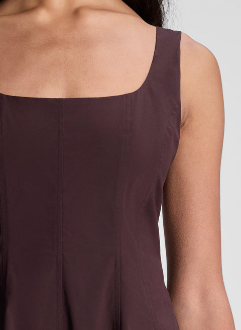 Close-up of a person wearing a dark brown sleeveless dress against a neutral background