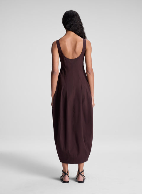 Back of woman wearing a brown maxi  dress with a plain background