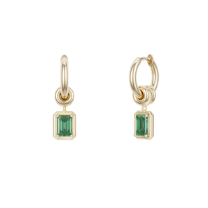 Ghost image of small, yellow gold hoop earring that features three yellow gold annulets, one with an emerald cut emerald stone charm. 