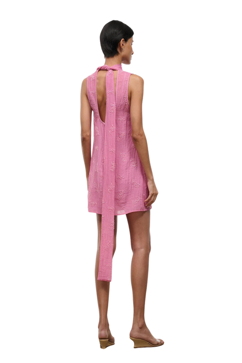 A woman wearing a pink high neck mini dress with beaded embellishments back angle with a tie