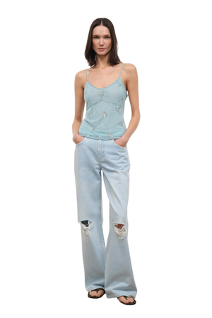 Woman wearing a light blue denim tank top with embellishments on a white background front