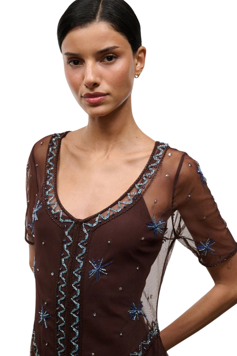 Woman wearing a brown sheer mini dress with embellishments on a white background close up