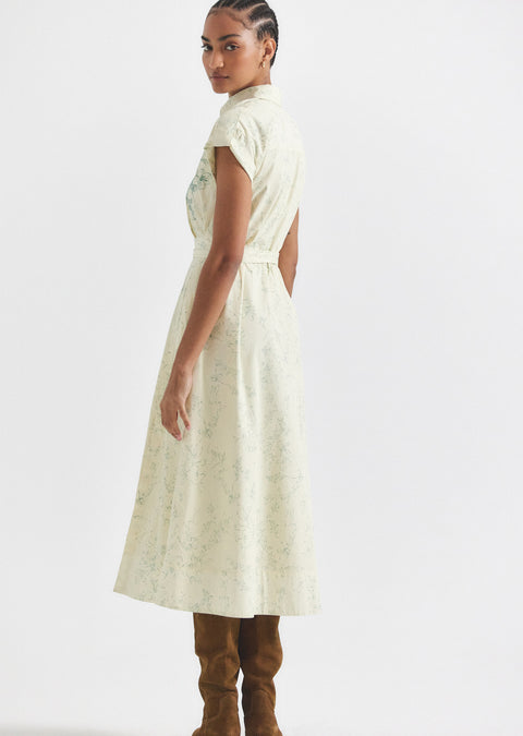 Woman shows side view of cream dress with green print.
