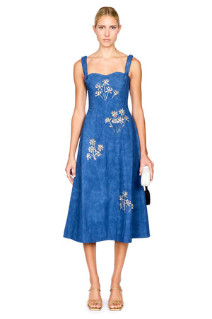 A woman modeling a blue midi dress with silver floral embroidery, standing against a plain white background.