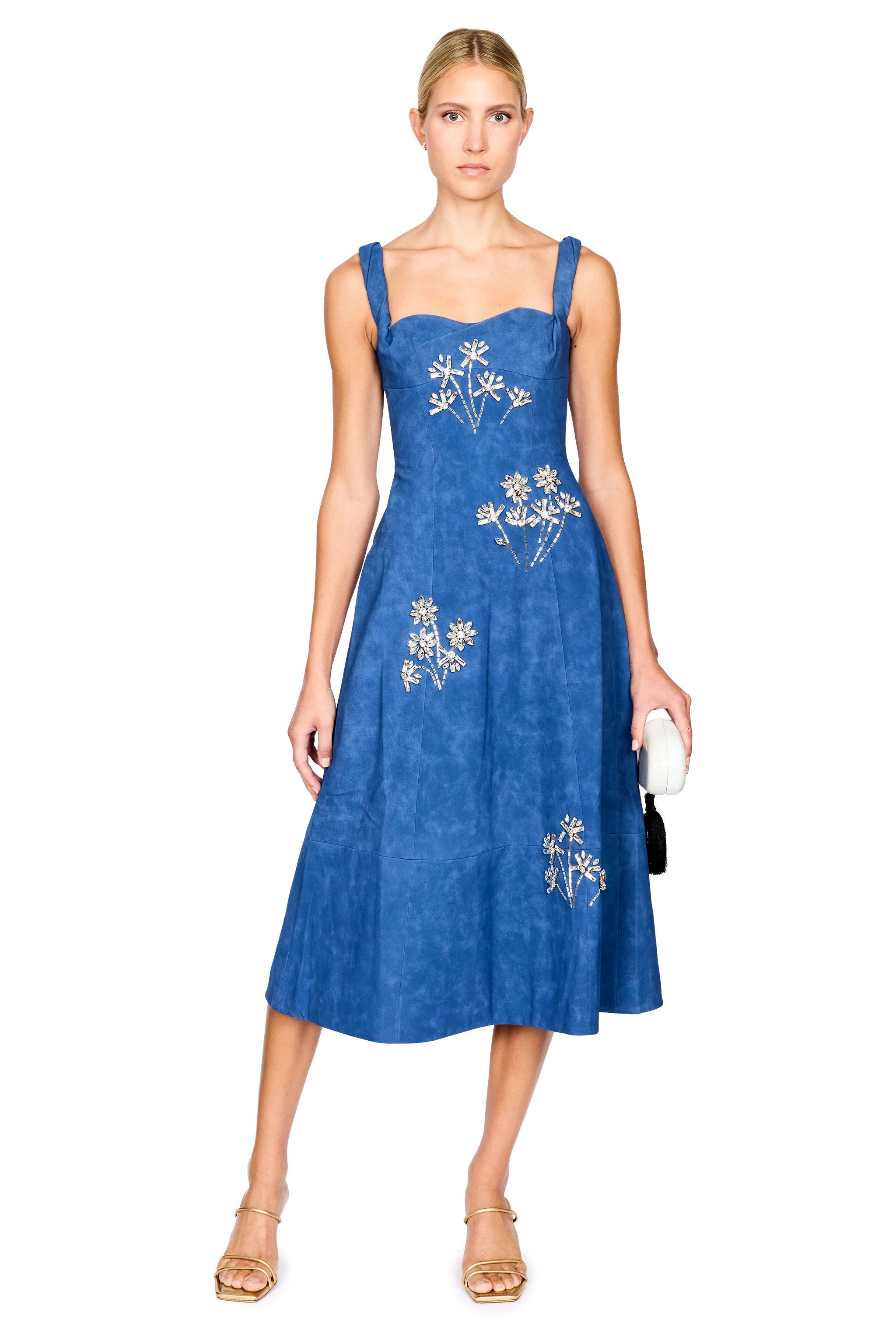 A woman modeling a blue midi dress with silver floral embroidery, standing against a plain white background.