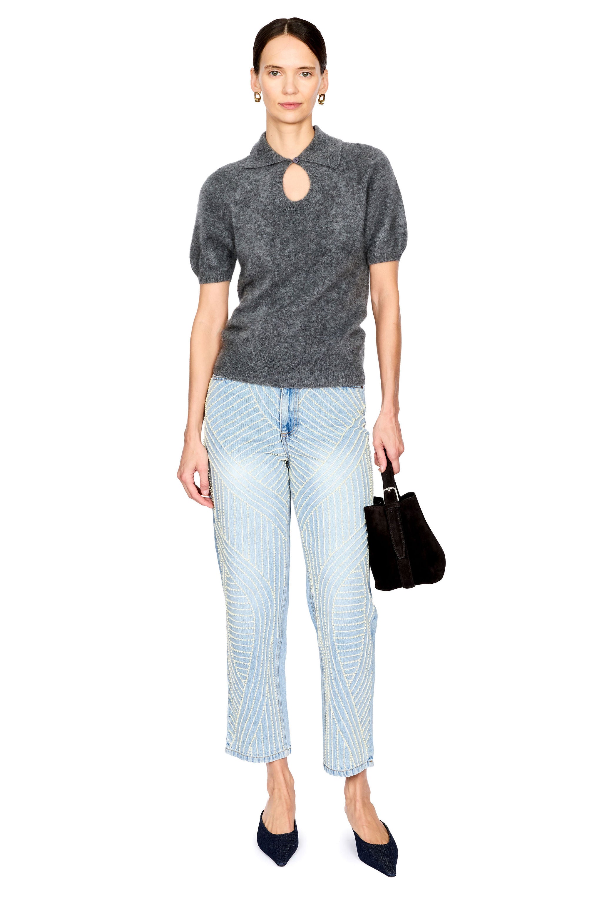 A model stands against a white background wearing a dark gray short-sleeve knit top with a keyhole cutout, light blue jeans with pearl detail, dark navy pointed shoes, and holding a dark brown handbag.