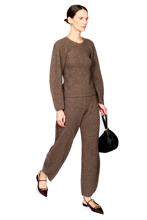A woman modeling a matching brown knit sweater and wide-leg trousers set, styled with dark pointed flats and a small black handbag against a plain white background.
