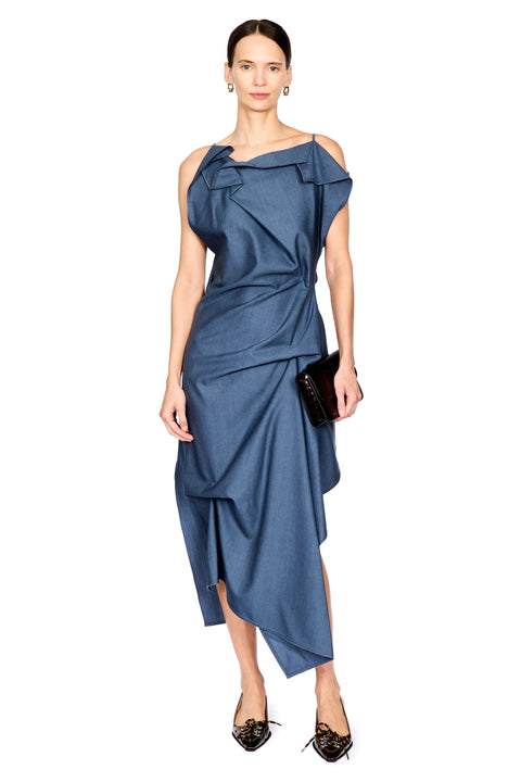 A model wearing a blue one-shoulder draped midi dress with a wrap-style skirt, holding a small black clutch against a plain white background.