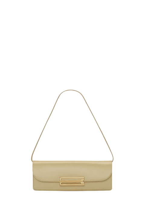 A light beige leather shoulder bag with a thin matching strap and a gold-tone metal accent on the front flap, shown against a plain white background.
