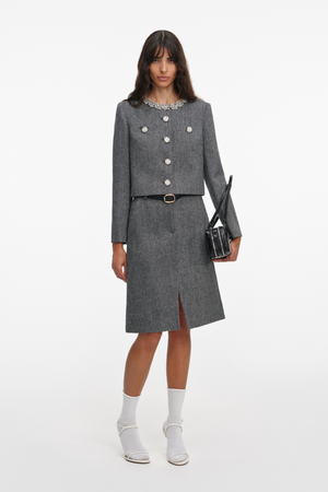 Woman wearing a gray herringbone outfit with a matching skirt and jacket on a white background