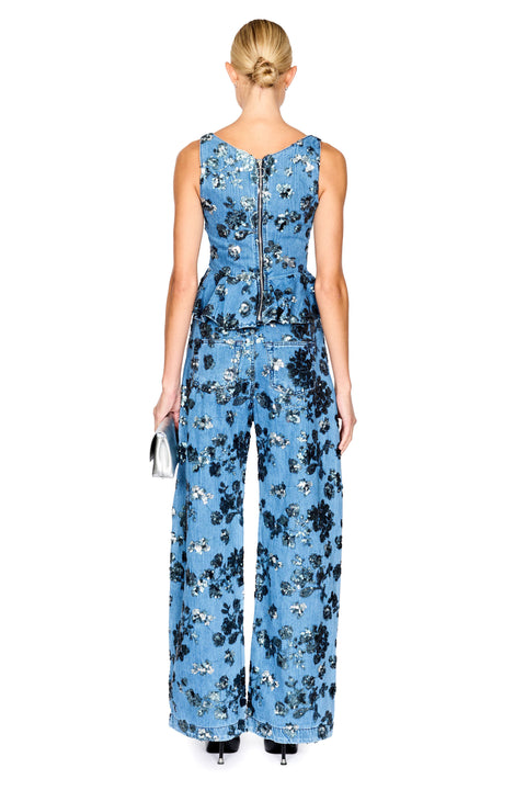A model wearing a sleeveless denim floral top with a peplum waist with matching jeans, photographed against a solid white background.