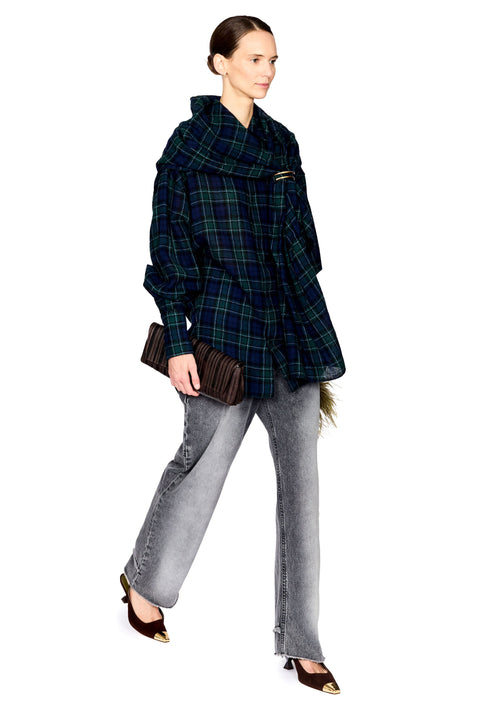 A model wearing a dark green and black plaid oversized wrap jacket, paired with light gray wide-leg jeans and brown pointed-toe heels, holding a brown pleated clutch against a solid white background.