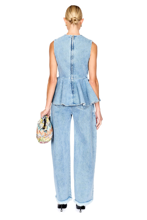 A woman shown from the back wearing a light blue denim sleeveless peplum top and matching wide-leg jeans, holding a small multicolor patterned handbag against a plain white background.