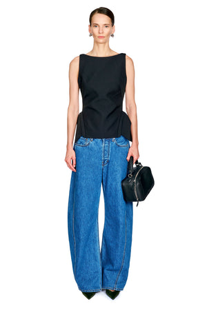 A model stands against a white background wearing a black sleeveless top, wide-leg blue jeans, and holding a small black handbag.
