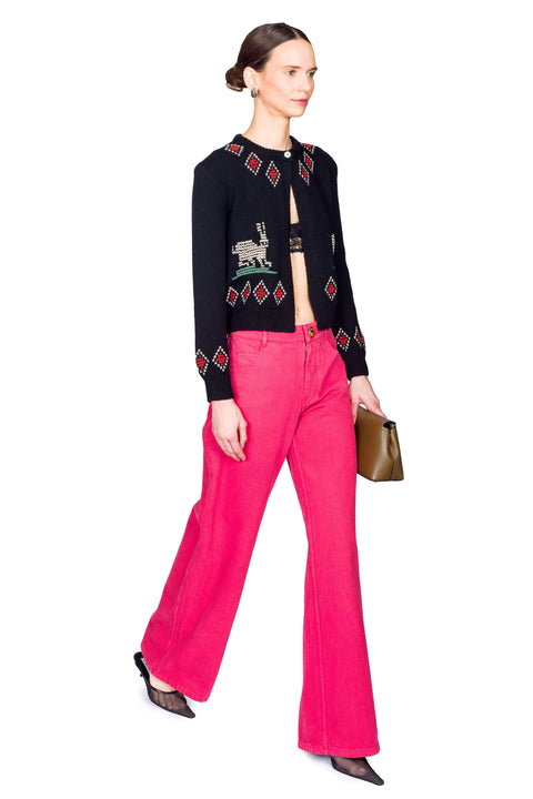 Woman wearing a black embroidered cardigan and pink pants on a white background stepping from the side.
