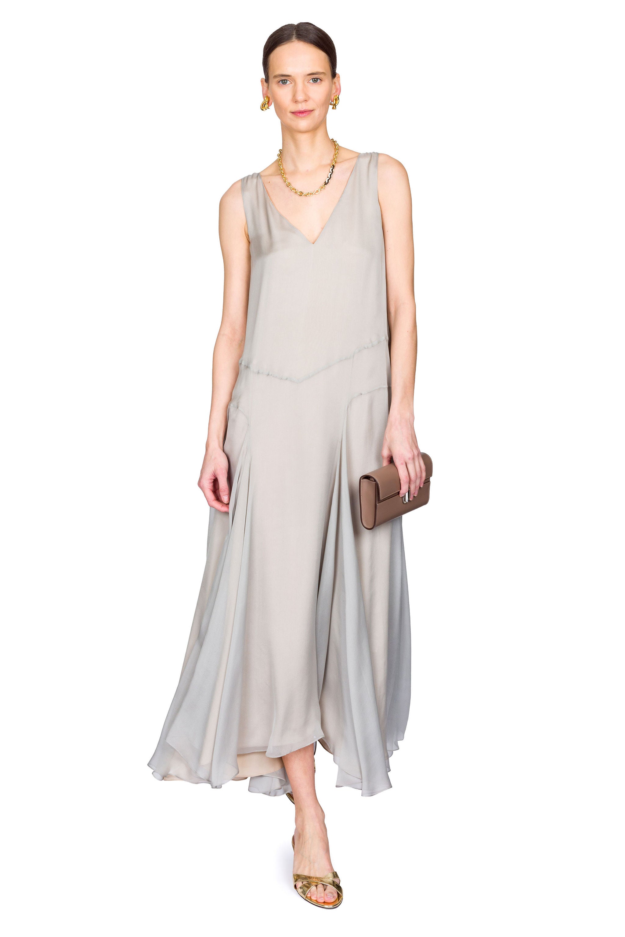 Woman wearing a light gray sleeveless dress holding a clutch on a white background