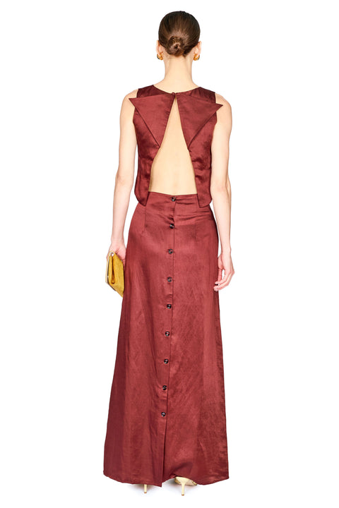 A model shown from the back wearing a sleeveless top with a dramatic open back and a long skirt with a button-down back, holding a small yellow clutch against a white background.