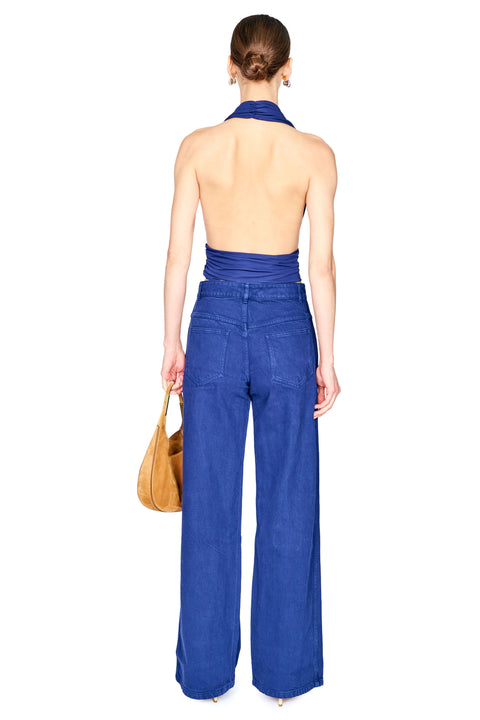 A woman shown from the back wearing a cobalt blue halter top with an open back and matching blue jeans