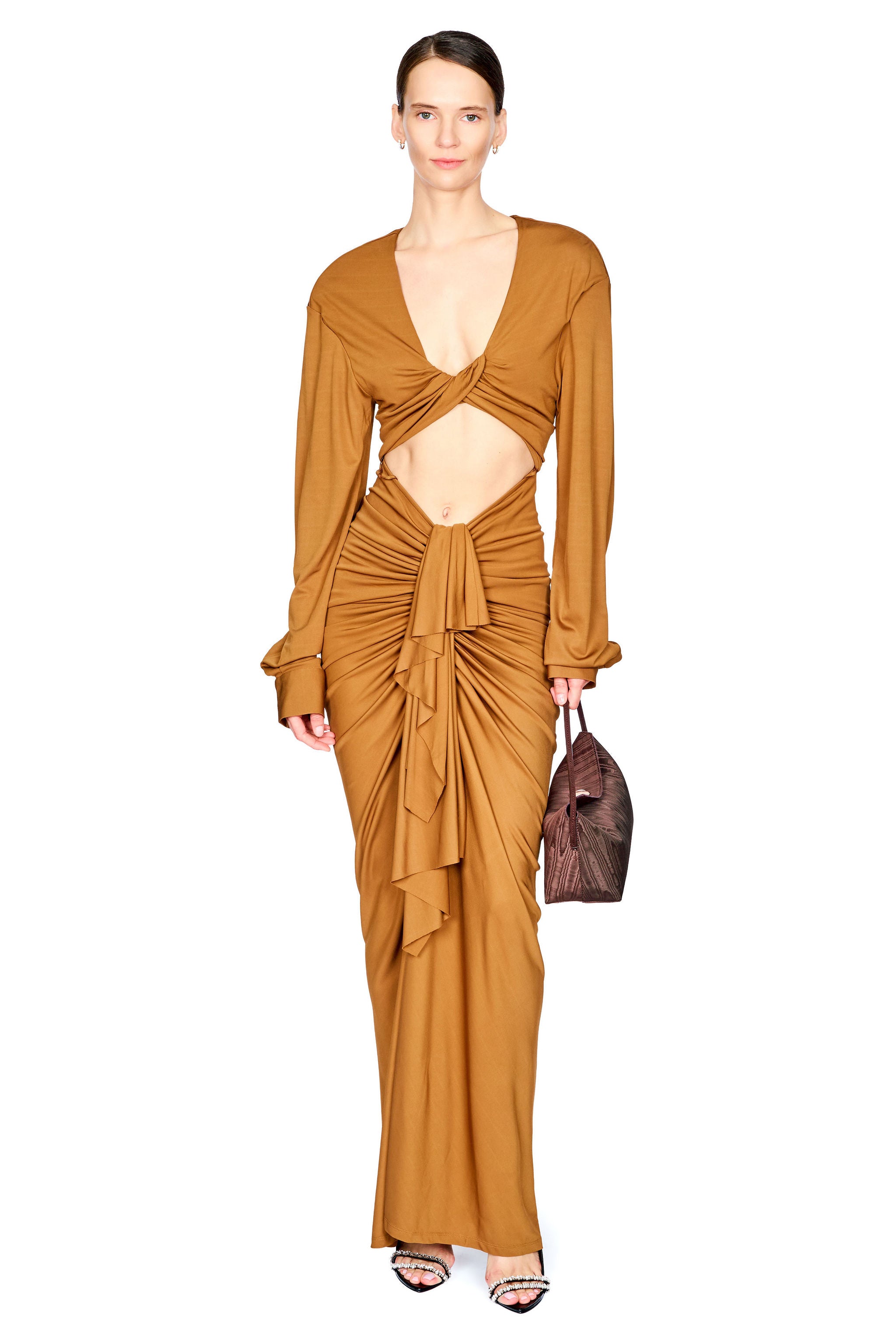 A woman on a white background wearing a cognac brown long dress with long sleeves, drapery from the waist down, and a cutout under the chest