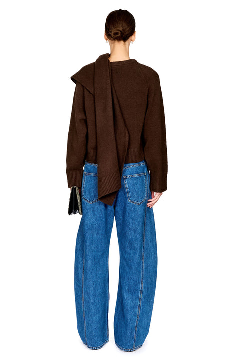 A model shown from the back wearing a dark brown draped knit sweater and wide-leg blue denim jeans against a plain white background.