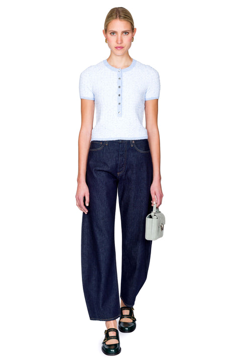 Woman wearing a light blue top with buttons and dark blue jeans on a white background stepping forward