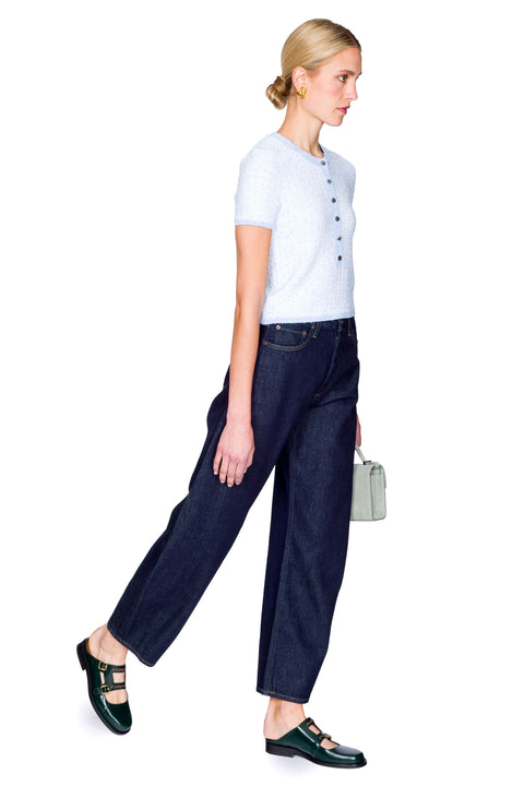 Woman wearing a light blue top with buttons and dark blue jeans on a white background from the side