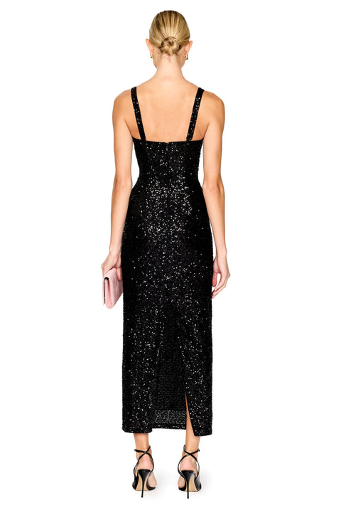 A woman shown from the back wearing a black sequined midi dress with thin straps, paired with black strappy heels and holding a pink clutch, against a plain white background.