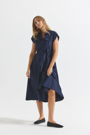 Woman stands in blue cotton belted midi dress.