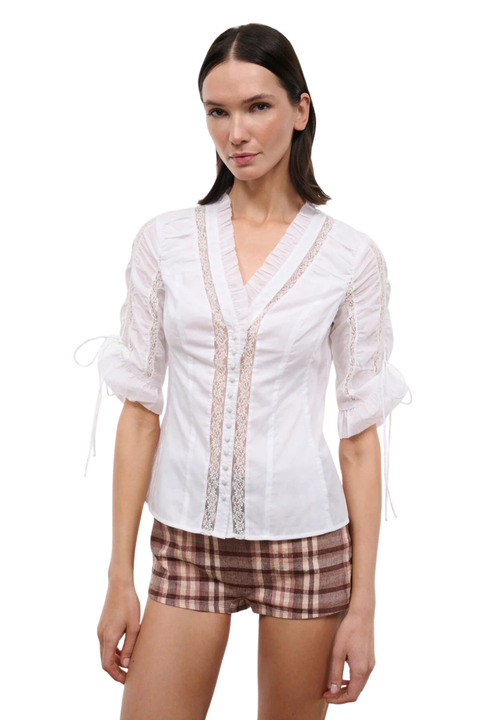 A woman wearing a white button-up top with cinched sleeves and lace detailing