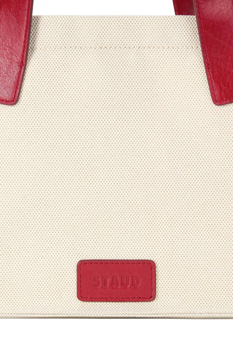 Close-up of a beige tote bag with red accents and 'STAUD' logo.
