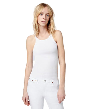 Woman wearing a white tank top and white pants against a plain background