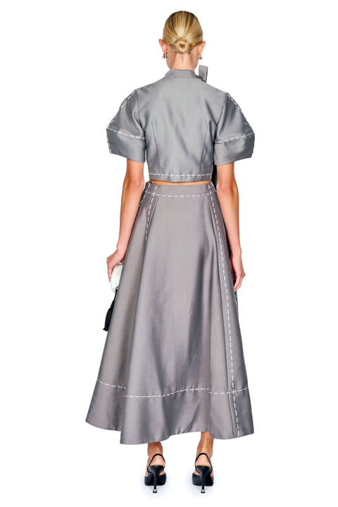 A model shown from the back wearing a gray two-piece set consisting of a short-sleeve cropped top and a matching high-waisted maxi skirt with white contrast stitching.