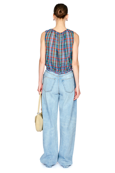 A model shown from the back wearing a sleeveless plaid top with red, blue, and green lines, paired with wide-leg light blue jeans and holding a small beige handbag against a white background.