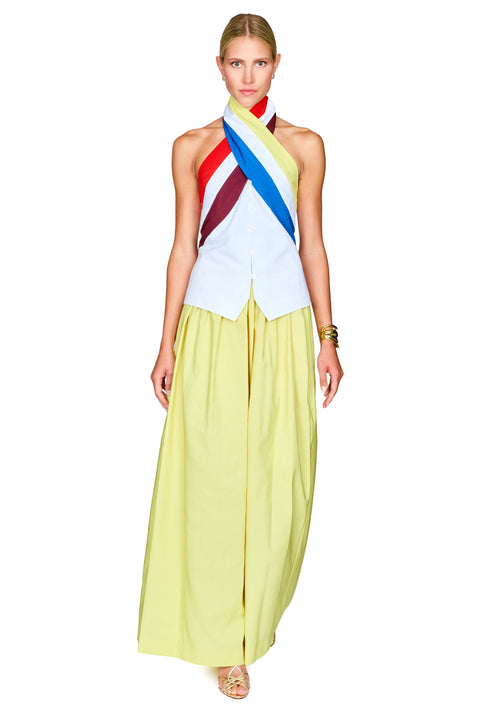 A model wearing a sleeveless halter top with diagonal red, yellow, blue, and white stripes, paired with a flowing pale yellow skirt.